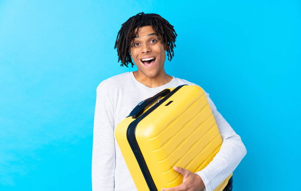 Jovem viajante afro-americano segurando uma mala com expressão facial surpresa e chocada
 - Foto, Imagem