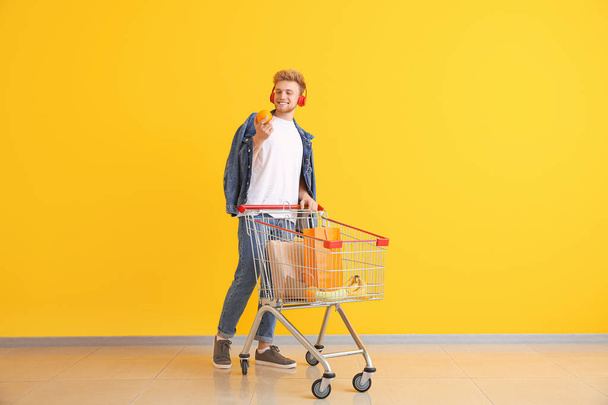 Young man with shopping cart near color wall - Φωτογραφία, εικόνα