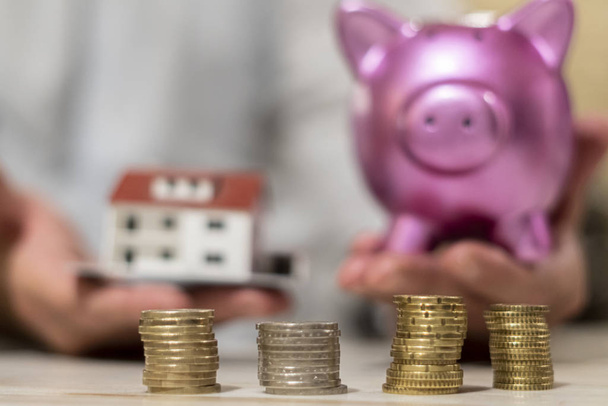Saving money and dreaming a new home concept. Coins, model house and piggy bank. Selective focus - Photo, Image
