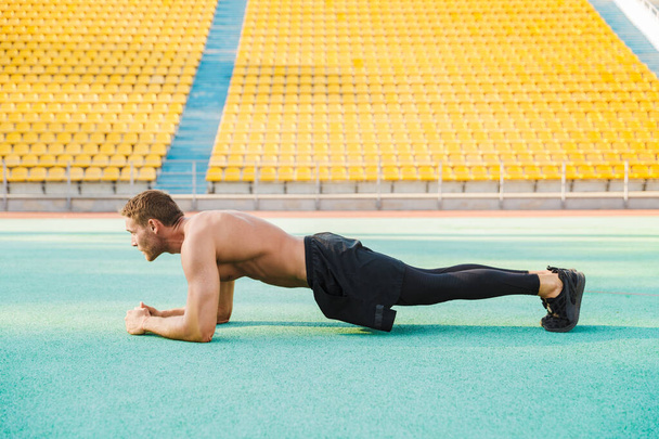 Image of muscular shirtless man doing plank exercise at sports s - Photo, Image