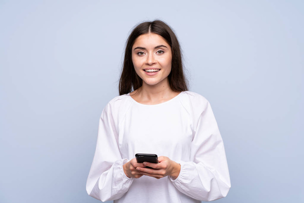 Молодая женщина на изолированном синем фоне отправляет сообщение или электронную почту с мобильного телефона - Фото, изображение