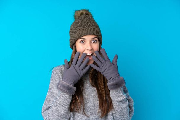 Подросток в зимней шляпе на изолированном синем фоне с неожиданным выражением лица - Фото, изображение