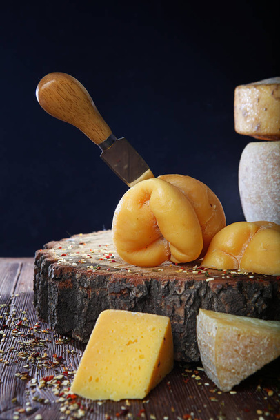 Large chunks of cheese on a wooden background. Cheese knife stuck into the head of the cheese. Still life concept. Preparation of craft cheeses in home production. - Photo, image
