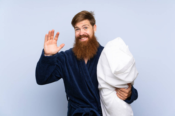 Redhead man in pajamas over isolated background saluting with hand with happy expression - Photo, Image