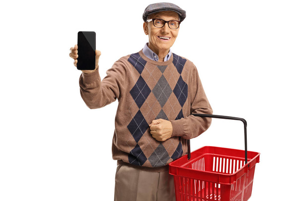 Elderly man showing a mobile phone and carrying a shopping baske - Фото, изображение