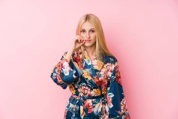 Young blonde woman wearing a kimono pajama with fingers on lips keeping a secret. - 写真・画像