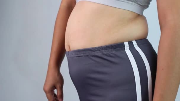 Detailní záběr ženské ruky štípající nadměrný břišní tuk izolovaný na šedém pozadí. Ženské tlusté břicho. Koncepce obezity a nadváhy. - Záběry, video