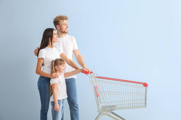 Family with empty shopping cart on color background - Fotó, kép