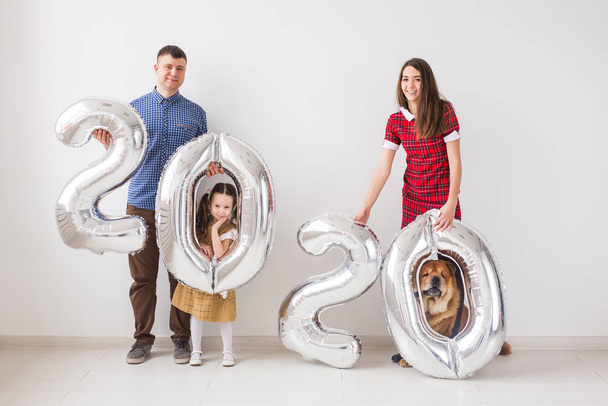 2020 Yeni Yıl geliyor - Köpekli mutlu aile kapalı alanda gümüş renkli sayılar tutuyor. - Fotoğraf, Görsel