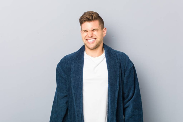 Young caucasian man wearing pajama laughs and closes eyes, feels relaxed and happy. - Foto, Imagen