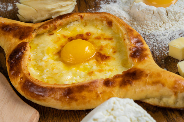 Adżarian Khachapuri z serem Adyghe i żółtkami jaj oraz plasterkami masła jest na drewnianej desce posypanej mąką. - Zdjęcie, obraz