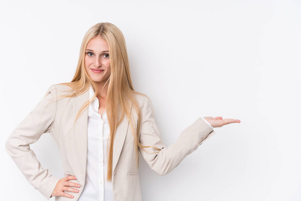 Young business blonde woman on white background showing a copy space on a palm and holding another hand on waist. - Fotografie, Obrázek