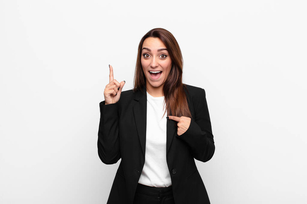 young pretty businesswoman feeling proud and surprised, pointing to self confidently, feeling like successful number one against white wall - Photo, image