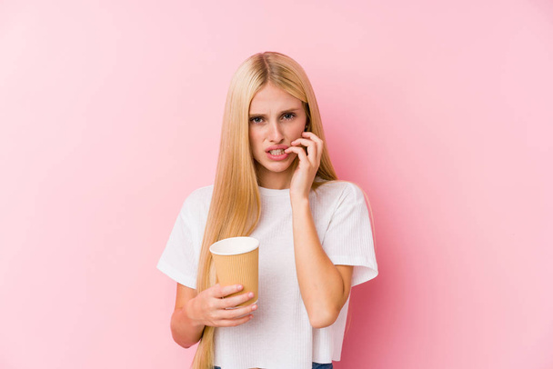 Young blonde girl holding a takeaway coffee biting fingernails, nervous and very anxious. - Foto, Imagen