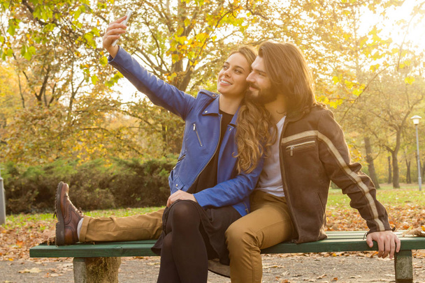 秋の色公園で携帯電話を使用してカップル. - 写真・画像