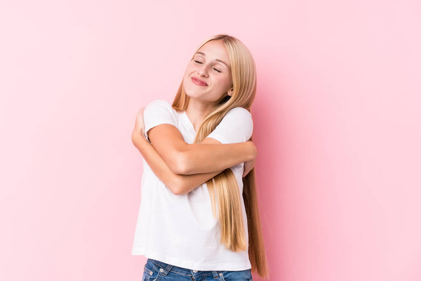 Young blonde woman on pink background hugs, smiling carefree and happy. - Photo, Image