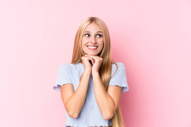 Young blonde woman on pink background keeps hands under chin, is looking happily aside. - Photo, image