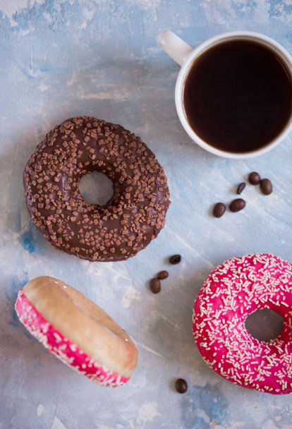 delicious donuts with pink icing and powder with a cup of aromatic coffee on a white wooden background. - Photo, Image