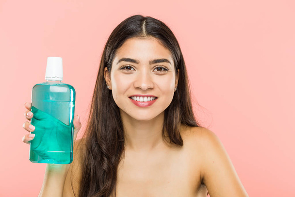 Young indian woman holding a mouthwash bottle happy, smiling and cheerful. - Photo, Image