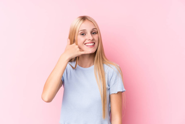 Young blonde woman on pink background showing a mobile phone call gesture with fingers. - Фото, зображення