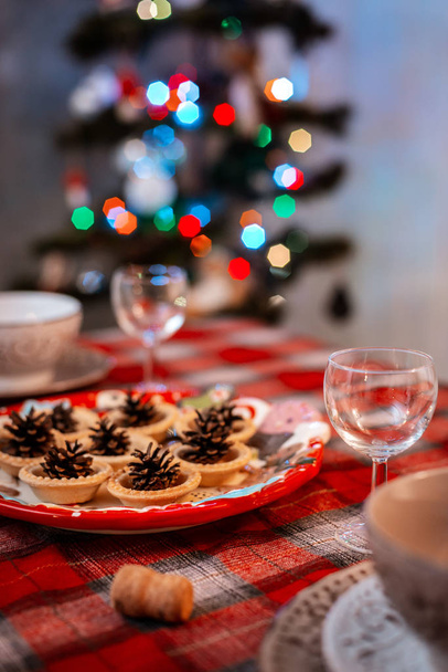 Traditionell geschmückter Weihnachtstisch. Kreative Dekoration der festlichen Tischkegel auf einem Teller auf dem Hintergrund von Bokeh-Lichtern. - Foto, Bild