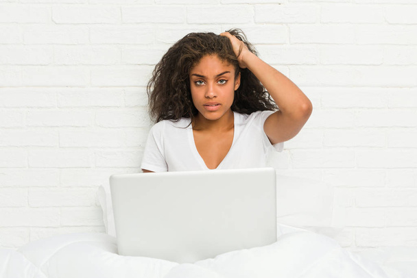 junge afrikanisch-amerikanische Frau sitzt auf dem Bett mit Laptop schockiert, sie erinnert sich an wichtige Treffen. - Foto, Bild