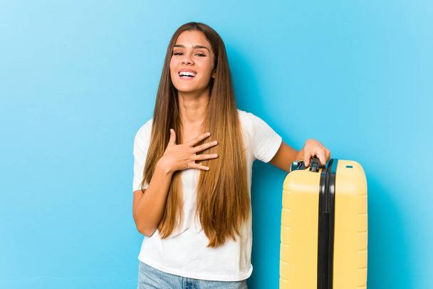 Young caucasian woman holding a travel suitcase laughs out loudly keeping hand on chest. - Fotoğraf, Görsel