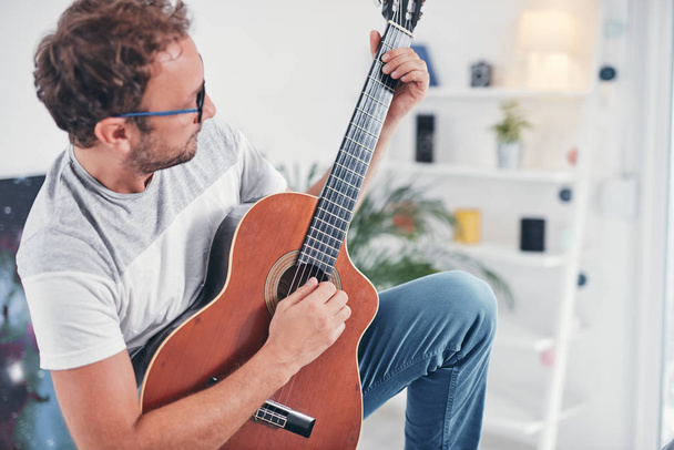 Человек, играющий на акустической гитаре в гостиной
. - Фото, изображение