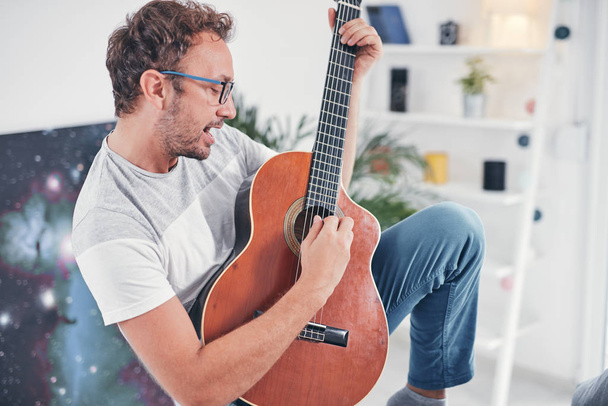 Muž hraje na akustickou kytaru v obývacím pokoji. - Fotografie, Obrázek