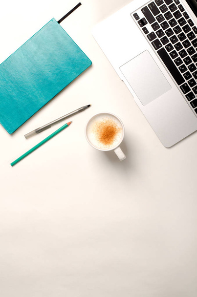 Werkruimte met laptop, turquoise notebook en kaneel koffie op witte tafel. Plat lag, top uitzicht - Foto, afbeelding