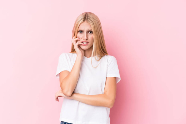Young blonde woman on pink background biting fingernails, nervous and very anxious. - Foto, Imagen