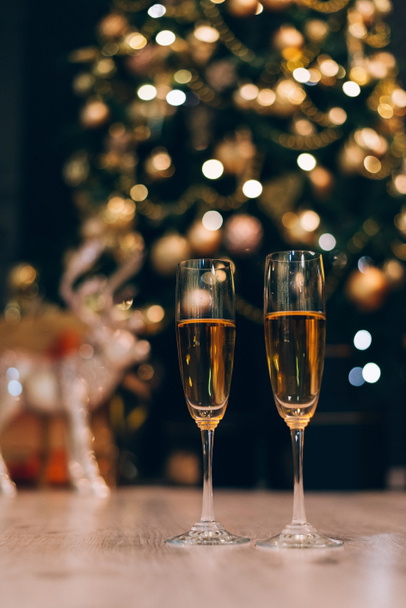 Twee glazen champagne staan op de wazig versierde kerstboom achtergrond. - Foto, afbeelding