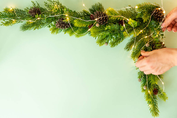 Woman making Christmas tree with corner decoration on green background, flat lay - Photo, Image