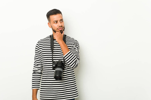Joven fotógrafo sudasiático mirando de lado con expresión dudosa y escéptica
. - Foto, imagen