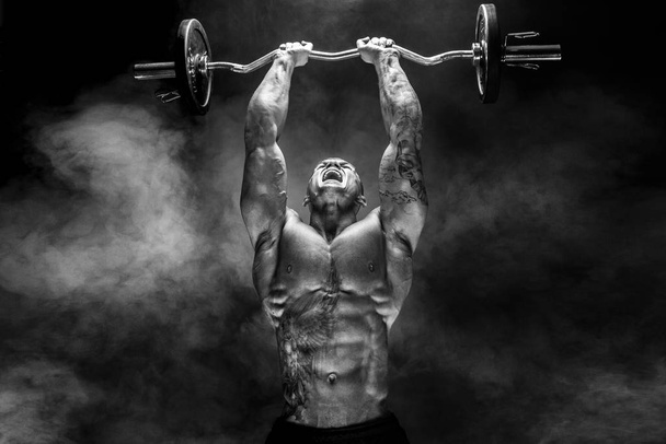 Strong sportsman lifting heavy dumbbell in smoke - Fotoğraf, Görsel