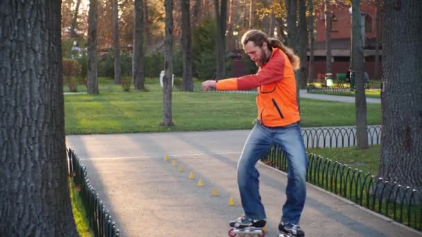 Sports man on roller skates deftly and successfully goes around cones for training, riding back and forth and showing the most complicated riding technique. Autumn training in a city park slow motion. - Footage, Video