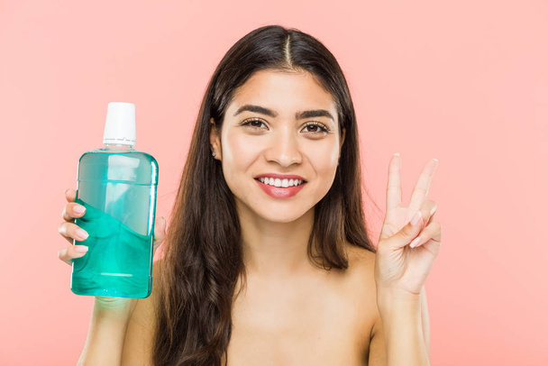 Young indian woman holding a mouthwash bottle showing number two with fingers. - 写真・画像
