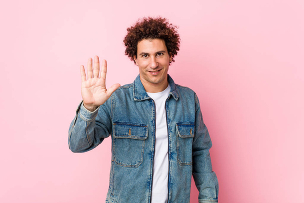 riccio maturo uomo indossa un denim giacca su sfondo rosa sorridente allegro mostrando numero cinque con le dita
. - Foto, immagini