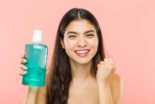 Young indian woman holding a mouthwash bottle cheering carefree and excited. Victory concept. - Photo, Image