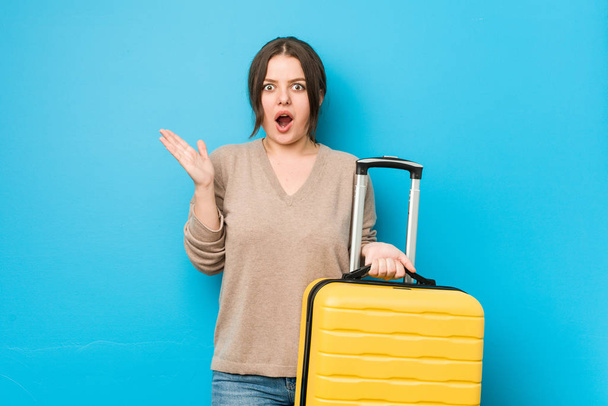 Mladá zakřivená žena drží kufr překvapený a šokovaný. - Fotografie, Obrázek