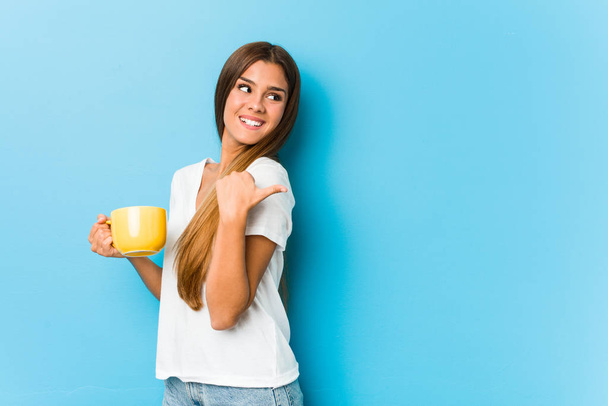 Молода біла жінка тримає кухоль для кави з великим пальцем подалі, сміється і безтурботний
. - Фото, зображення