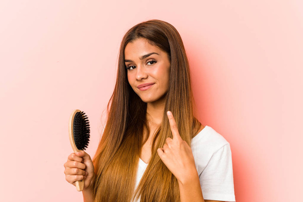 Mulher caucasiana jovem segurando uma escova de cabelo apontando com o dedo para você como se convidando chegar mais perto
. - Foto, Imagem