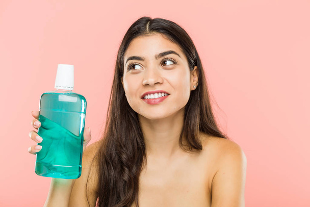 Young indian woman holding a mouthwash bottle smiling confident with crossed arms. - Photo, Image