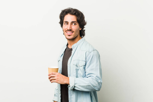 młody cool człowiek pijąc kawę patrzy na bok uśmiechnięty, wesoły i przyjemny. - Zdjęcie, obraz