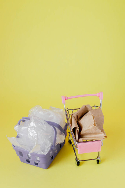 polythene and paper bags in a shopping basket on a yellow background - 写真・画像