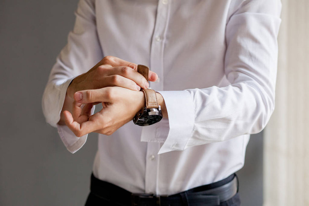 The groom looks at his watch to check the time. The watch is worn on the man's hand. Groom's morning preparation before wedding - Photo, image