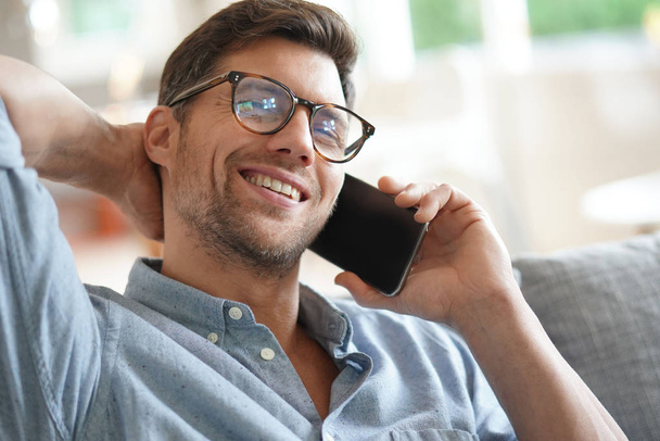 Smiling man relaxing in sofa, talking on phone - Photo, image