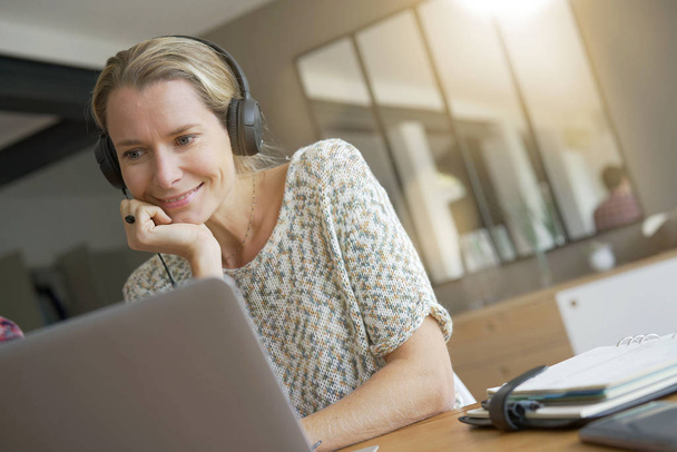 νεαρή ξανθιά γυναίκα που εργάζεται σε ένα γραφείο με ακουστικά - Φωτογραφία, εικόνα