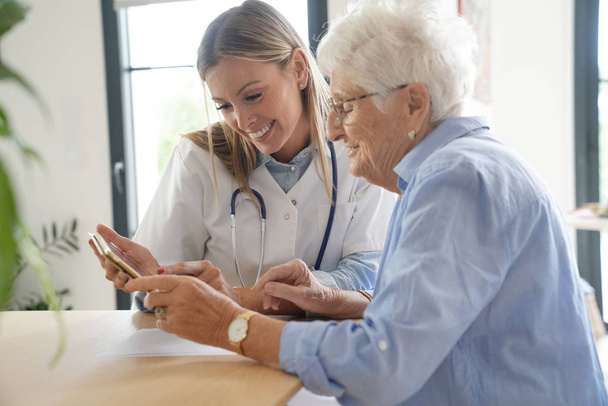 Elderly woman with nurse at home looking at tablet - Photo, image
