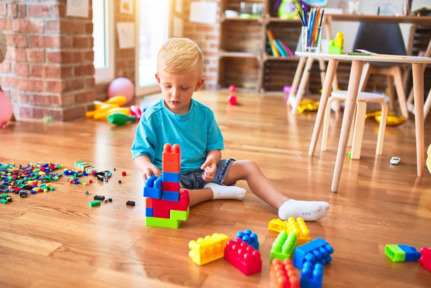 Anaokulunda oyuncak bloklarıyla oynayan beyaz bir çocuk. Anaokulu çocuğu oyun odasında kule inşa etmekten mutlu. - Fotoğraf, Görsel
